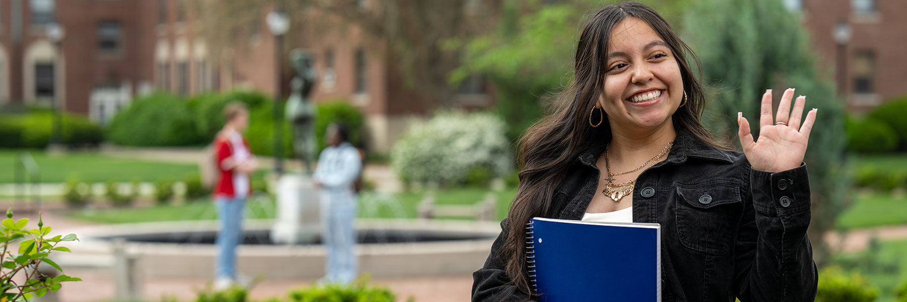student walking on campus waving