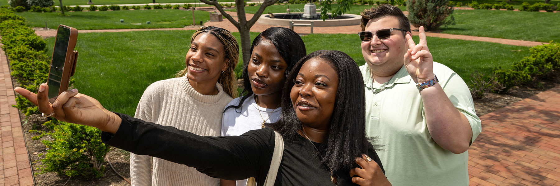 four students on campus smiling while taking a group selfie with a cell phone