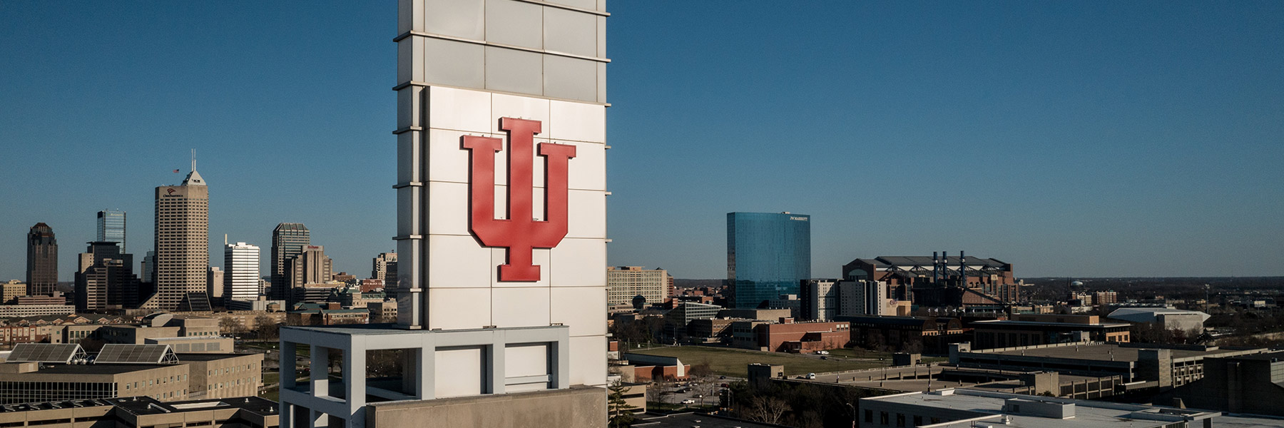 IU trident sits above the Campus Center bell tower at IU Indianapolis, with the Indianapolis skyline in the background